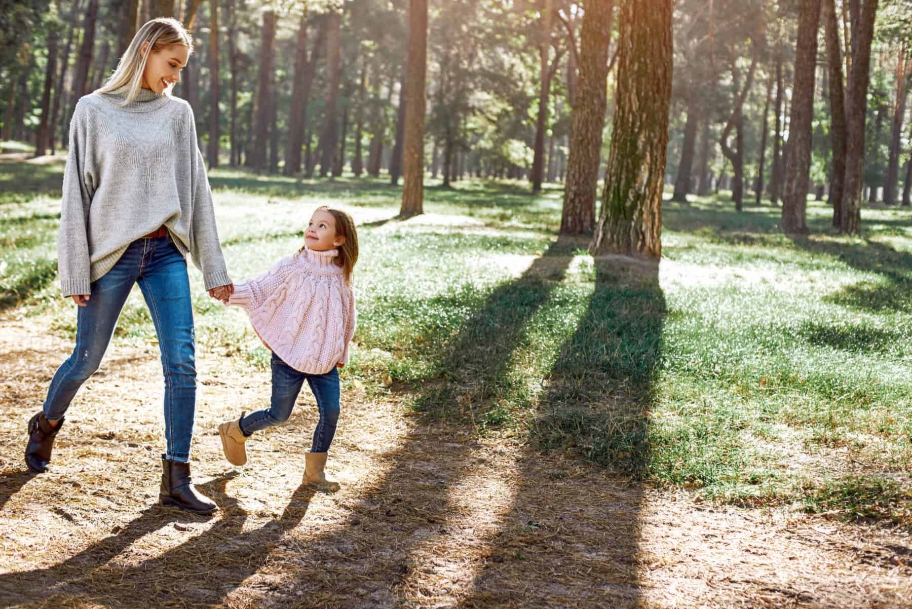 Happy, stylish little curly girl is walking with her beautiful mother in forest