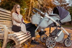 Stylish mom with stroller talking on the phone while sitting on bench in the park while the child is sleeping