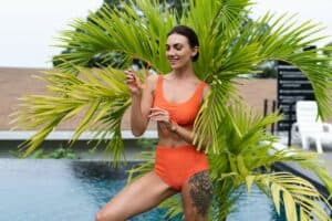 Beautiful european women in two pieces orange bikini swimsuit in perfect shape, good body, tanned, with trendy sunglasses outside at tropical swimming pool and palm leaf tree