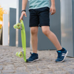 Cum alegi primul sneaker de brand pentru copilul tău close-up-legs-blue-sneakers-with-green-skateboard-active-urban-lifestyle-youth-training-hobby-activity-active-outdoor-sport-kids-child-skateboarding-