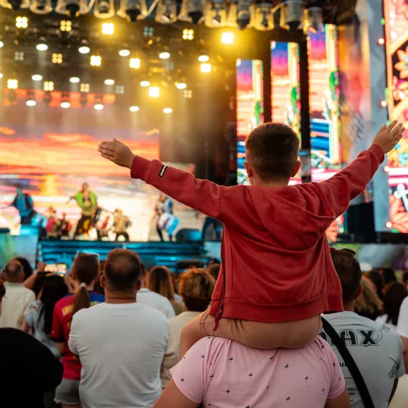 Baiat pe umerii părintelui cu brațele deschise spre scena principală a festivalului Nibiru.