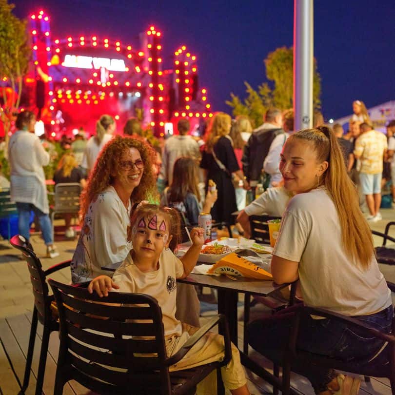 Fetiță pictată pe față stând la masă pe o terasă în aer liber la festivalul Nibiru.