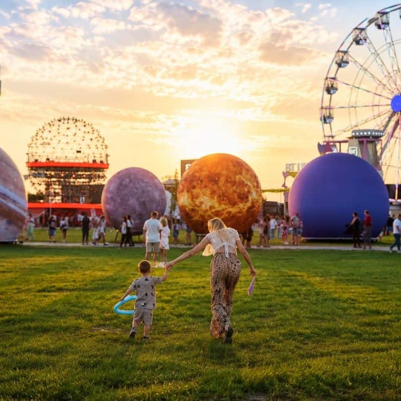 Mamă și copil mergând pe iarbă printre decorțiuni gigantice cu planete la festivalul Nibiru.